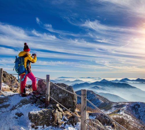 Young woman hiker taking photo with smartphone on mountains peak in winter.
